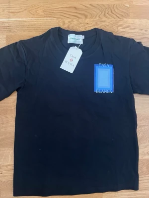 Svart t-shirt från Casablanca - Svart t-shirt från Casablanca med blått tryck och logga på bröstet. Klassisk rund halsringning och korta ärmar. Perfekt för en stilren och modern look.