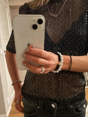 Svart mesh topp med glitterprickar - Snygg svart mesh topp med glittriga prickar och korta ärmar. Toppen är transparent och har en hög hals, perfekt för att styla lager på lager. Materialet känns lätt och luftigt, vilket ger en trendig look.