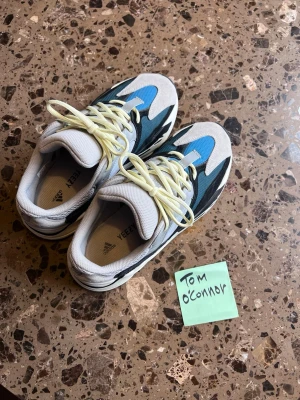Yeezy Boost 700 Wave Runner sneakers - Säljer ett par Yeezy Boost 700 Wave Runner sneakers från Adidas. Skorna har en mix av grått, svart, blått och vitt med gula skosnören och chunky sula. Materialet är mesh, mocka och läder för en riktigt modern look.