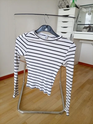 Randig ribbad topp från H&M Divided - Säljer en vit ribbad topp från H&M Divided med svarta horisontella ränder. Toppen har lång ärm, rund halsringning och är i en slim passform. Perfekt att styla med jeans eller kjol för en enkel och snygg look.