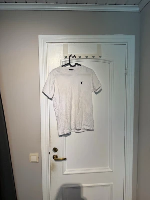 Vit t-shirt från Polo Ralph Lauren - Klassisk vit t-shirt från Polo Ralph Lauren i 100% bomull. T-shirten har korta ärmar och den ikoniska lilla broderade loggan på bröstet. Perfekt basic-plagg med normal passform och rund hals.