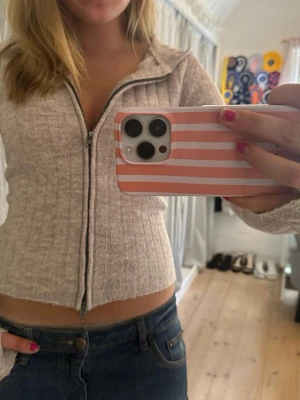 Beige ribbad ziptröja med luva - Säljer en beige ribbad ziptröja med luva och långa ärmar. Tröjan är croppad och har en mjuk, stretchig känsla. Perfekt att slänga över ett linne eller t-shirt för en chill look.