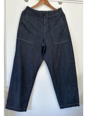 UNIQLO - Mörkblå raka jeans med stora fickor - storlek M (W28-29) - Stilrena mörkblå jeans från UNIQLO i storlek M / W28-29, motsvarande ett midjemått på mellan 70-74cm. Tidlös och smickrande modell med resår i midjan och knappstängning. Byxorna har två snedställda fickor framtill och två påsydda bakfickor. Kontrasterande sömmar ger en fin detalj. Finvävd stabil denim i 100% bomull, så bra material som andas. Mycket gott skick, som nya!