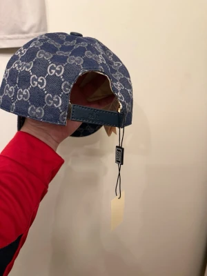 Blå denimkeps  - Säljer en blå keps i denim med det klassiska GG-monogrammet över hela kepsen. Justerbar rem bak i läder och snygg böjd skärm. Perfekt för dig som vill ha en trendig accessoar med lyxig känsla och streetwear-vibe.