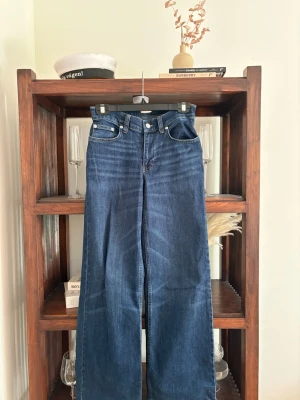 Mörkblå raka jeans med mid midja - Säljer ett par mörkblå jeans med raka, vida ben och mid midja. Klassisk femficksmodell med silverfärgade nitar och knapp. Jeansen har en tidlös look och är tillverkade i denim med snygg tvätt. Perfekta för en avslappnad och trendig stil.
