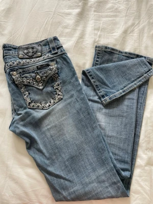 Miss Me jeans  - Säljer ett par skitsnygga blå jeans från Miss Me med snygga slitningar och broderade detaljer på bakfickorna. Dem är low waist, bootcut och har dekorativa knappar.🫶🏻29cm rakt över midjan och innerbensmått 78cm