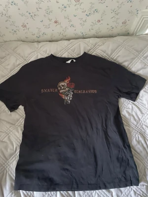 Svart t-shirt Skater Generation H&M - Cool svart t-shirt från H&M med tryck av en dödskalle och eld samt texten 'Skater Generation' på bröstet. Klassisk passform och korta ärmar, perfekt för en avslappnad streetstil. Tillverkad i mjuk bomull för skön känsla hela dagen.