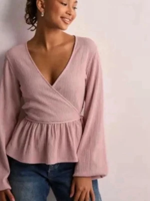 Ljusrosa omlottopp med knyt - Supersöt ljusrosa omlottopp med v-ringning och långa ärmar. Toppen har ett band i midjan för knyt och ett lätt rynkat fall nedtill. I xs men passar även mig som har S/M, går att justera mycket pga knytet!