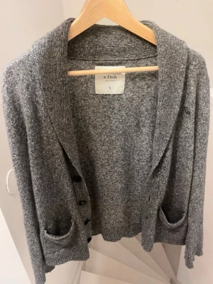 Grå kofta från Abercrombie & Fitch - Mysig gråmelerad kofta från Abercrombie & Fitch med två framfickor och knappar framtill. Koftan har en normal passform, ribbade muddar och mjukt material som passar perfekt till lager på lager. Klassisk och enkel design som funkar till det mesta.