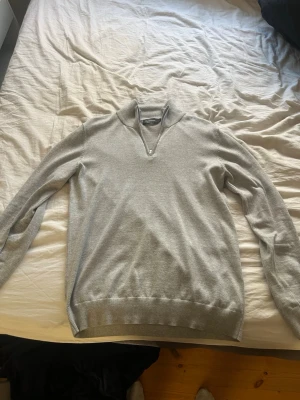 Ljusgrå halvzip tröja Dressmann - Superskön ljusgrå tröja från Dressmann i Supima-bomull. Halvzip-dragkedja vid halsen och ribbade muddar vid ärmslut och nederkant. Perfekt för lager på lager och enkel att matcha med jeans eller chinos.