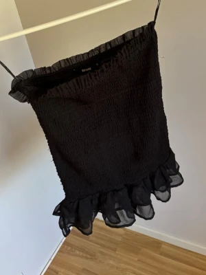 Svart volangkjol från Bik Bok - Svart kjol från Bik Bok med smockad midja och volangkant nedtill. Kjolen är figurnära och har tunna, genomskinliga volanger i mesh. 