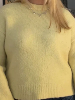 Stickad tröja gul - Mysig gul stickad tröja med rund halsringning och ribbade muddar vid ärmslut och nederkant. Tröjan har en avslappnad passform och är perfekt för lager på lager. Materialet ser ut att vara en mjuk ull- eller akrylblandning.