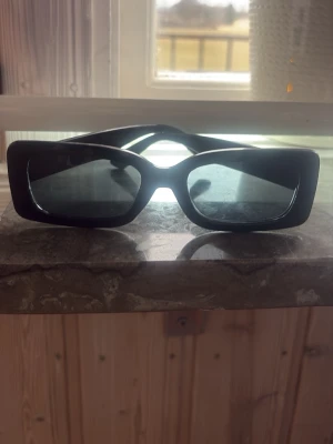 Svarta rektangulära solglasögon - Snygga svarta solglasögon med breda, rektangulära bågar och mörka glas. Perfekt accessoar för dig som vill ha en trendig och stilren look. Passar till alla outfits och ger en cool vibe.