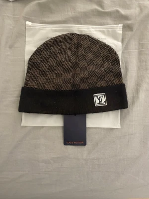 Brun mössa med rutmönster - Snygg brun mössa  med klassiskt rutmönster och vikt kant. Märkt med framtill och etikett på insidan. Tillverkad i mjukt stickat material som känns lyxigt och trendigt. Perfekt accessoar för dig som gillar exklusiv streetstyle.