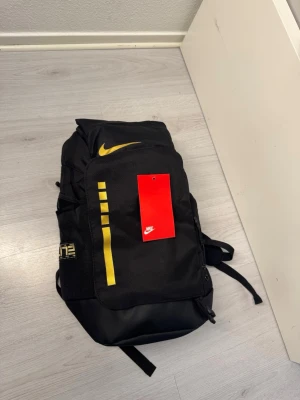 Svart Nike elite bag ryggsäck med gula detaljer - Snygg svart ryggsäck från Nike med gula detaljer och logga. Ryggsäcken har flera fack, dragkedja och justerbara axelband. Tillverkad i slitstarkt material och har en modern, sportig design. Perfekt för skola eller träning. Inte använd. Kom DM för fler bilder :)