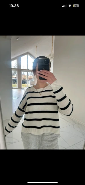 Vit stickad tröja med svarta ränder - Säljer en vit stickad tröja med svarta horisontella ränder. Tröjan har rund halsringning, långa ärmar och ribbstickade muddar. Den är i en avslappnad passform och passar perfekt till jeans eller mjukisbyxor. Materialet känns mjukt och bekvämt.