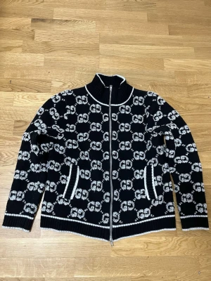 Svartvit stickad ziptröja från Gucci - Säljer en svart stickad ziptröja från Gucci med vit GG-logga över hela tröjan.  Den är ny har inga skador den är strl S pris kan diskuteras och tar byten beror på vad det är.