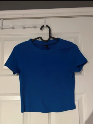 T-shirt  - Stilren blå croppad topp med korta ärmar och rund hals. Toppen är ribbad och sitter snyggt tight mot kroppen, vilket ger en trendig och avslappnad look. Perfekt att matcha med både jeans och kjol för en enkel men stilren outfit.(ifrån shein) 
