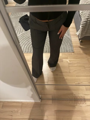 Grå kostymbyxor med vita ränder - Säljer ett par grå kostymbyxor med smala vita kritstrecksränder. Byxorna har rak passform, normal midja och klassisk knappgylf. Perfekta för en stilren och trendig look. Jag är 163 cm lång. De är helt rena och fina inga skador/skavanker precis som nya🌸