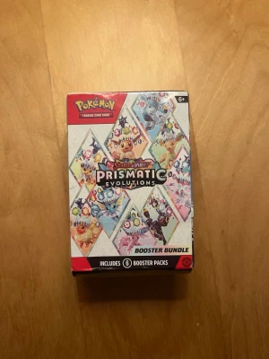 Pokémon Prismatic Evolutions Booster bundle - Säljer en Pokémon Scarlet & Violet Prismatic Evolutions Booster Bundle med 6 booster packs. Förpackningen är färgglad med illustrationer av olika Pokémon och passar samlare och fans av Pokémonkort. Perfekt för att utöka din samling. (Obs ej äkta).