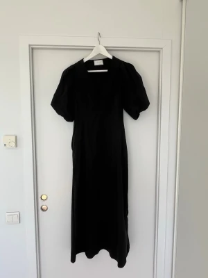 Svart långklänning från Neo Noir - Stilren svart långklänning från Neo Noir med puffiga korta ärmar och v-ringad hals. Klänningen har en elegant, enkel design. Använd en gång!