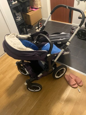 Bugaboo Donkey syskonvagn lila/blå - Säljer en Bugaboo Donkey syskonvagn i lila och blått med svarta och vita detaljer. Vagnen har två sittdelar, justerbart handtag i svart läderimitation och stora hjul för enkel körning. Perfekt för två barn och smidig att använda i vardagen.