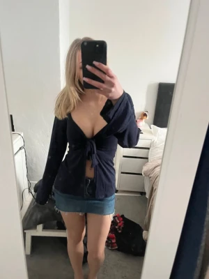 Design by si topp - Trendig mörkblå topp med lång ärm och djup v-ringning. Toppen har en snygg knytning framtill som ger en feminin touch och är lätt croppad. Perfekt att styla med kjol eller jeans för en cool look.