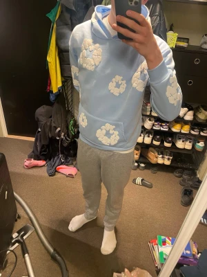 Ljusblå denim tears hoodie - Säljer en ljusblå hoodie med vita molnliknande mönster över hela tröjan. Hoodien har en stor huva och en klassisk magficka framtill. Perfekt för dig som gillar en chill och unik stil. Materialet känns mjukt och bekvämt. Storleken är smal men sitter som en oversized medium, hör av er om ni har frågor!!!!