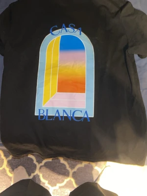 Casa Blanca svart t-shirt med tryck - Svart t-shirt från Casa Blanca med färgglatt grafiskt tryck av ett fönster i blått, gult, orange och rosa på både bröstet och ryggen. Klassisk passform och rund halsringning. Perfekt för dig som gillar streetwear och unika prints.