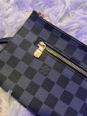 Rutigt clutch-inspirerad handväska - Snygg handväska i svart och mörkgrått rutmönster med guldfärgade detaljer och dragkedja framtill. Väskan har en handledsrem och är tillverkad i ett tåligt konstlädermaterial. Perfekt för dig som gillar stilrena accessoarer med en lyxig touch.