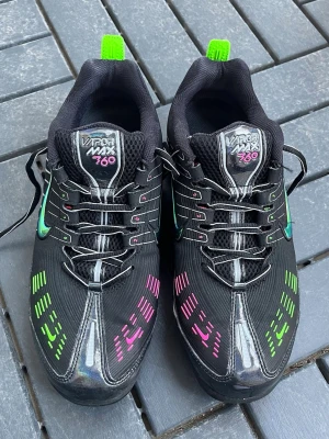 Nike Vapormax 360 svart neon - Nike Vapormax 360 sneakers i svart med neonrosa och neongröna detaljer på ovandelen. Skon har en futuristisk design med reflekterande linjer, meshmaterial och en synlig Air-sula. Swoosh-loggan är i metallic och skorna har svarta snören med vita detaljer.