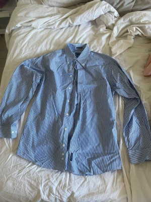 Blårandig skjorta från GANT storlek M - Klassisk blårandig skjorta från GANT i modellen Pinpoint Oxford Sport Fit. Skjortan har långa ärmar, vit knappstängning och en snygg krage. Tillverkad i bomull för en skön och luftig känsla. Perfekt för en clean och stilren look. Storlek M