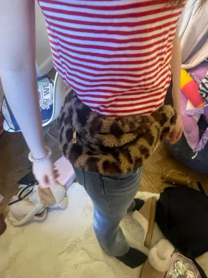 Leopardmönstrad fluffig handväska - Säljer en supermjuk och fluffig handväska med leopardmönster. Väskan har en rund form och dragkedja i guld. Perfekt för dig som vill sticka ut och addera lite extra attityd till din outfit.