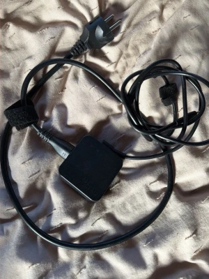 Svart ASUS laptop-laddare - En svart laptop-laddare från ASUS med fyrkantig adapter och lång kabel. Utrustad med kardborreband för enkel kabelhantering. Passar till flera ASUS-datorer och har en klassisk stickkontakt.
