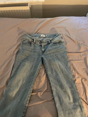 Ljusblå flared jeans från 152 - Säljer ett par ljusblå jeans med flared passform och klassisk femficksdesign. Jeansen har en snygg broderad detalj på bakfickan och är tillverkade i slitstark denim. Perfekta för en avslappnad och trendig look.