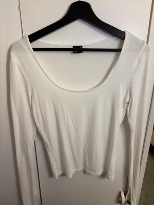 Vit långärmad topp Gina Tricot - En vit långärmad topp från Gina Tricot i modellen soft touch jersey top. Toppen har en djup rundringning och är tillverkad i ett mjukt material som sitter skönt mot kroppen. 