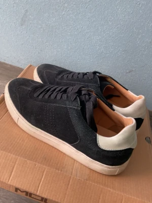 Svarta sneakers i mocka från MOLS - Snygga svarta sneakers från MOLS i mjuk mocka med vita sulor och svarta skosnören. Klassisk låg modell med diskreta sömmar och bekväm innersula. Perfekta för en stilren och avslappnad look.