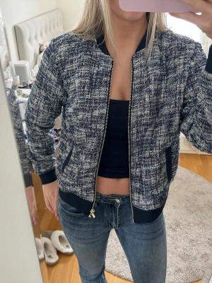 Blåvit bomberjacka från Holly & White - Snygg blåvit bomberjacka från Holly & White med grovt vävt tyg och guldfärgad dragkedja. Jackan har ribbade muddar, två fickor med mörkblå detaljer och en klassisk bomberkrage. Perfekt för dig som vill ha en trendig och unik look. Står storlek L men jag bär i vanliga fall S/M!!