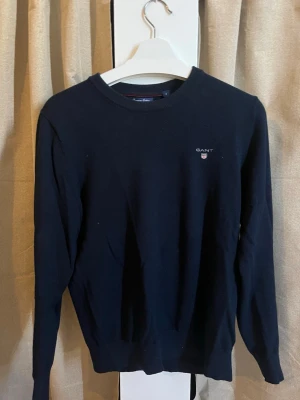 Gant Crewneck Tröja i Premium Cotton – Marinblå – Storlek S - Säljer en stilren och klassisk crewneck-tröja från Gant i färgen marinblå. Tröjan är en del av deras "Premium Cotton"-serie, vilket innebär att den är gjord i en mjuk och hållbar bomullskvalitet som håller formen bra.  Märke: Gant  Storlek: S (Small)  Färg: Marinblå (Navy)  Material: 100% Premium Cotton  Skick: Mycket bra skick! Inga hål, fläckar eller tvättblekning. Sparsamt använd och väl omhändertagen.  En perfekt baströja som passar till både skjorta och jeans eller mer avslappnat!