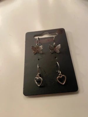 Söta örhängen fjäril & hjärta silverfärg - Två par örhängen i silverfärg, ett par med detaljerade fjärilar och ett par med öppna hjärtan. Perfekta för dig som gillar gulliga och stilrena accessoarer. Helt oanvända och ej äkta silver. 10kr styck eller båda för 17kr 🫶