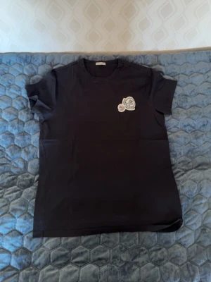 Svart Moncler t-shirt med logga - Snygg svart t-shirt från Moncler med klassisk rund hals och korta ärmar. På bröstet sitter Monclers ikoniska logga som en patch. Perfekt basplagg för en clean och stilren look. Storlek S men passar xs! 