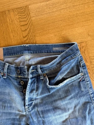 Dondup jeans - Säljer ett par klassiska blå jeans från Dondup med knappgylf och fem fickor. Jeansen har slitna detaljer vid fickorna och kontrastsömmar. Tillverkade i denim med en snygg tvättad look och patch bak i midjan. Hör av er vid funderingar!