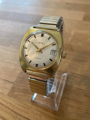 1970 BKN Swiss Mekanisk 35mm Herrur - Säljer ett snyggt vintage armbandsur från sent 60- eller 70-tal. En guldpläterad herrklocka från ovanliga schweiziska BKN i nära nyskick enligt bilder. Det mekaniska urverket (std. 974) fungerar bra, originalarmband i stål och flexband som passar alla, guldpläterad, datumvisare, vattentät, stöttålig, 17 juveler osv.  Begagnat värde: < 800 SEK Mitt pris: 589 SEK  Skickas alltid snabbt och spårbart. Skriv vid frågor och se gärna mina andra annonser!   GRATIS: För återkommande kunder erbjuder jag…