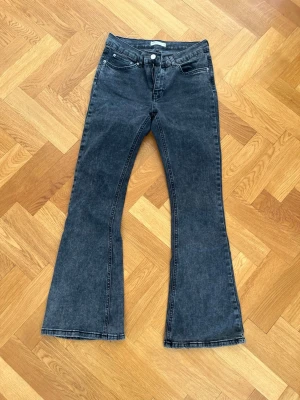 Svarta bootcut jeans med medelhög midja - Säljer ett par svarta bootcut jeans med medelhög midja och klassisk femficksmodell. Jeansen har utsvängda ben och är tillverkade i ett mjukt denimtyg. Perfekta för dig som gillar en retroinspirerad look.