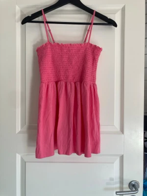 Rosa smockad linnetopp med volang - Säljer en söt rosa linnetopp med smockad överdel och tunna axelband. Toppen har en volangkant upptill och ett rynkat, luftigt fall nedtill. Perfekt för varma dagar och enkel att matcha med jeans eller kjol.