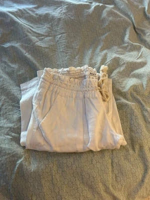 Linnebyxor från Roxy - Säljer ett par ljusbeige linnebyxor från Roxy med avslappnad passform och resår i midjan. Perfekta för en chill och bekväm stil under varma dagar.