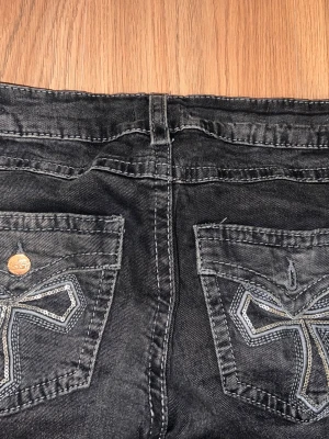 Svarta jeans med broderade bakfickor - Säljer ett par svarta jeans med snygga broderade detaljer på bakfickorna och kontrastsömmar. Jeansen har raka ben och en klassisk femficksmodell. Perfekta för dig som vill ha en unik touch på din outfit.