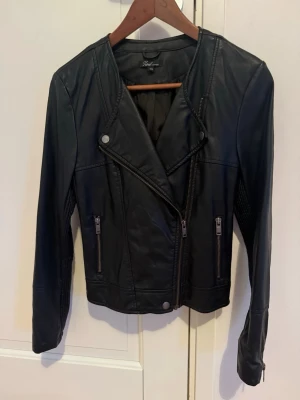 Svart skinnjacka från MQ - Snygg svart skinnjacka från Zoul Edition, MQ med asymmetrisk dragkedja, två framfickor med dragkedjor och detaljerade sömmar. Jackan har dragkedjor vid ärmsluten och en klassisk bikerstil som ger en cool look.