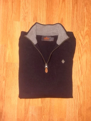 Morris Merino Ull Halfzip Tröja - Snygg mörkblå Merino ull tröja från Morris med halv dragkedja och grå insida på kragen. Tröjan har en liten broderad logga på bröstet och ribbade muddar. Perfekt för dig som gillar klassisk och stilren design.