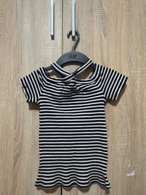 Randig topp med twistad hals - Säljer en svartvit ribbad topp med korta ärmar och twistad detalj vid halsen. Toppens ränder ger en snygg och trendig look, och materialet är stretchigt och bekvämt. Perfekt för dig som gillar att sticka ut med din stil. Den passar 152-xxs är mycket stretchig i material. Använd fåtal gånger, perfekt för sommarn:)